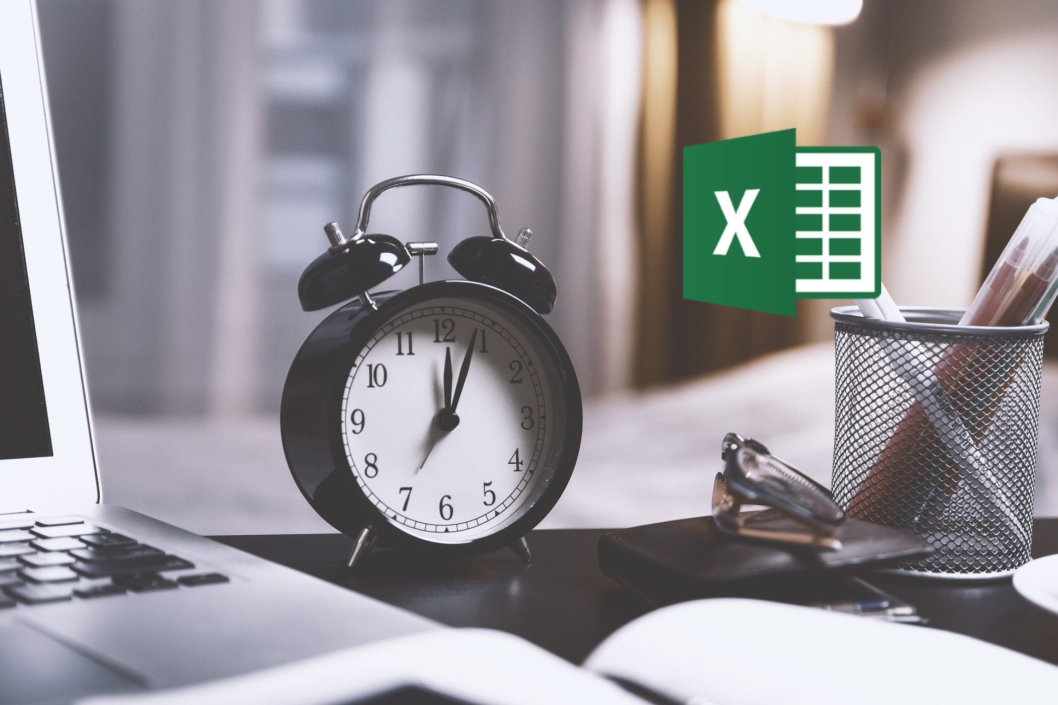 A work desk with a laptop, pen holder, and small clock on top, with the Excel icon hovering above the desk.