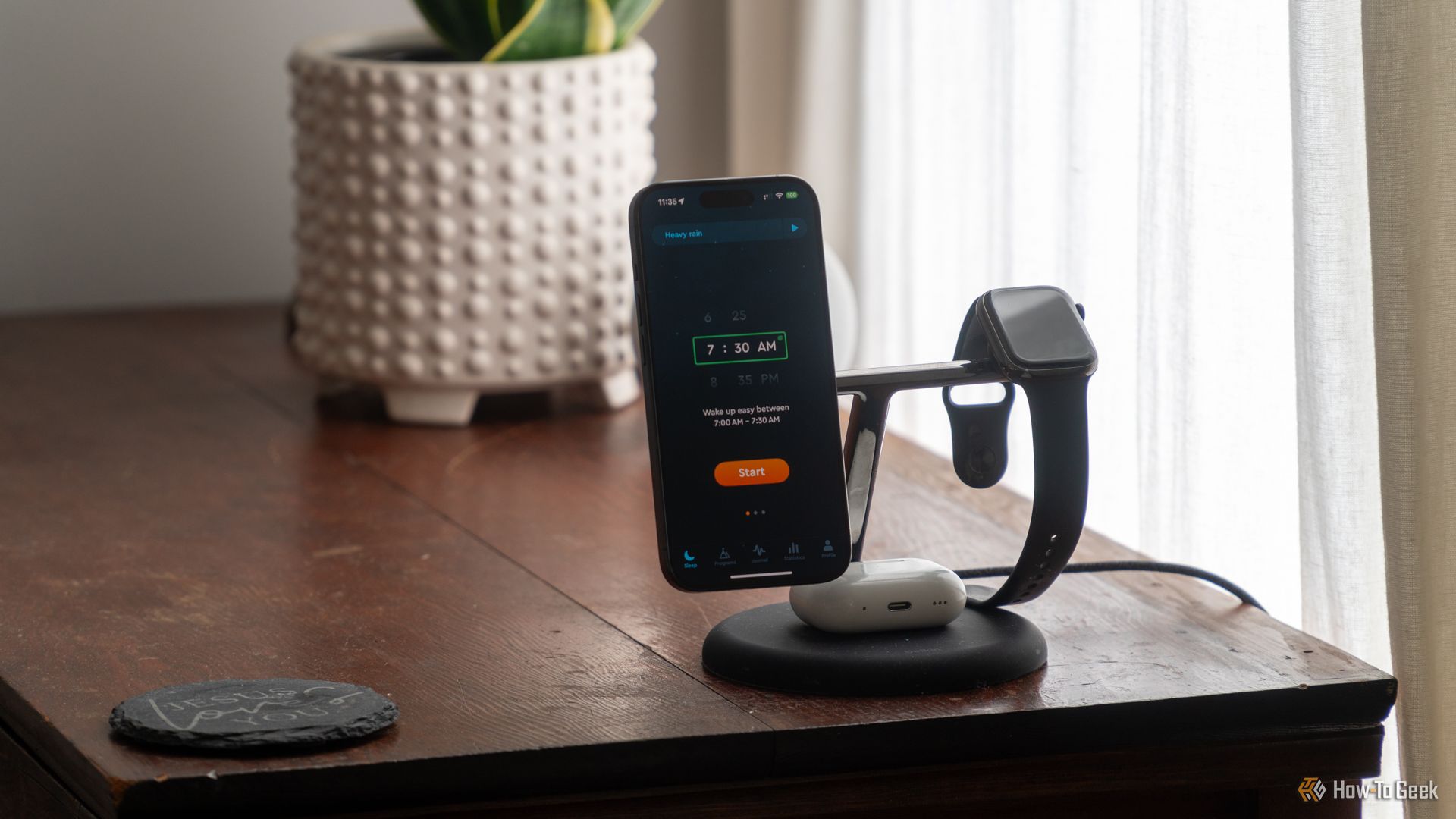 The Sleep Cycle app opened on an iPhone 15 Pro docked on a charger on a bedside table with an Apple Watch next to it and AirPods Pro below it.