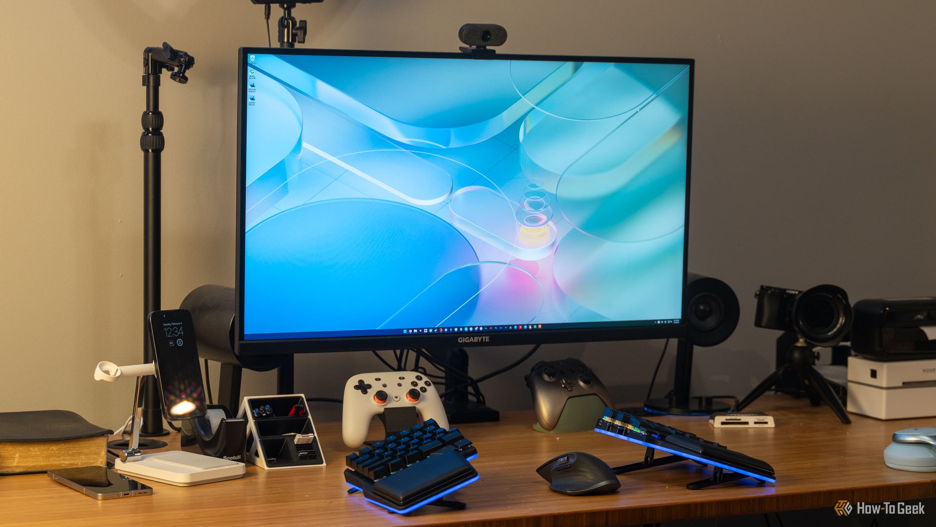 A GIGABYTE M32U 16:9 4K gaming monitor on a desk with a keyboard, controllers, and other accessories.