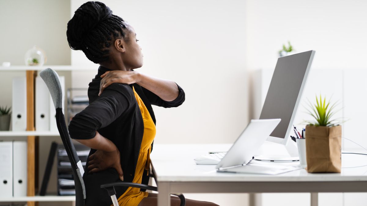 Woman sitting in office chair and rubbing her shoulders and back in response to pain.