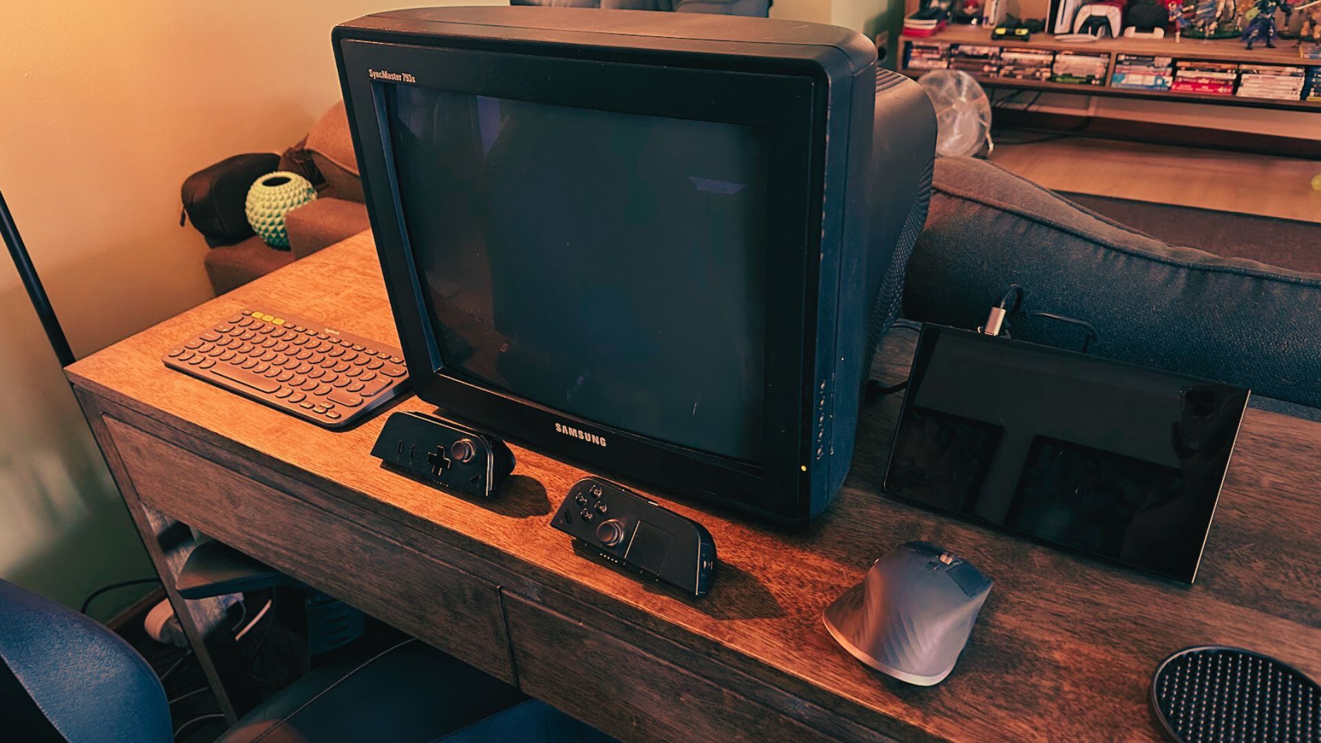 A CRT computer montor hooked up to a handheld PC with a mouse and keyboard on a desk and some controllers.