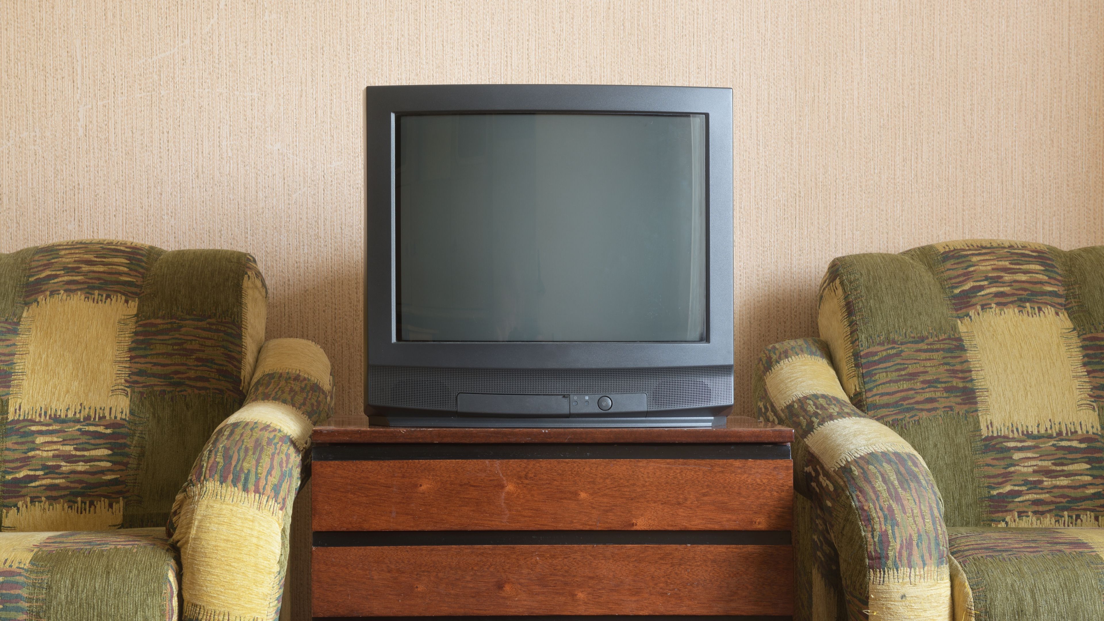 A CRT television next to some old chairs.