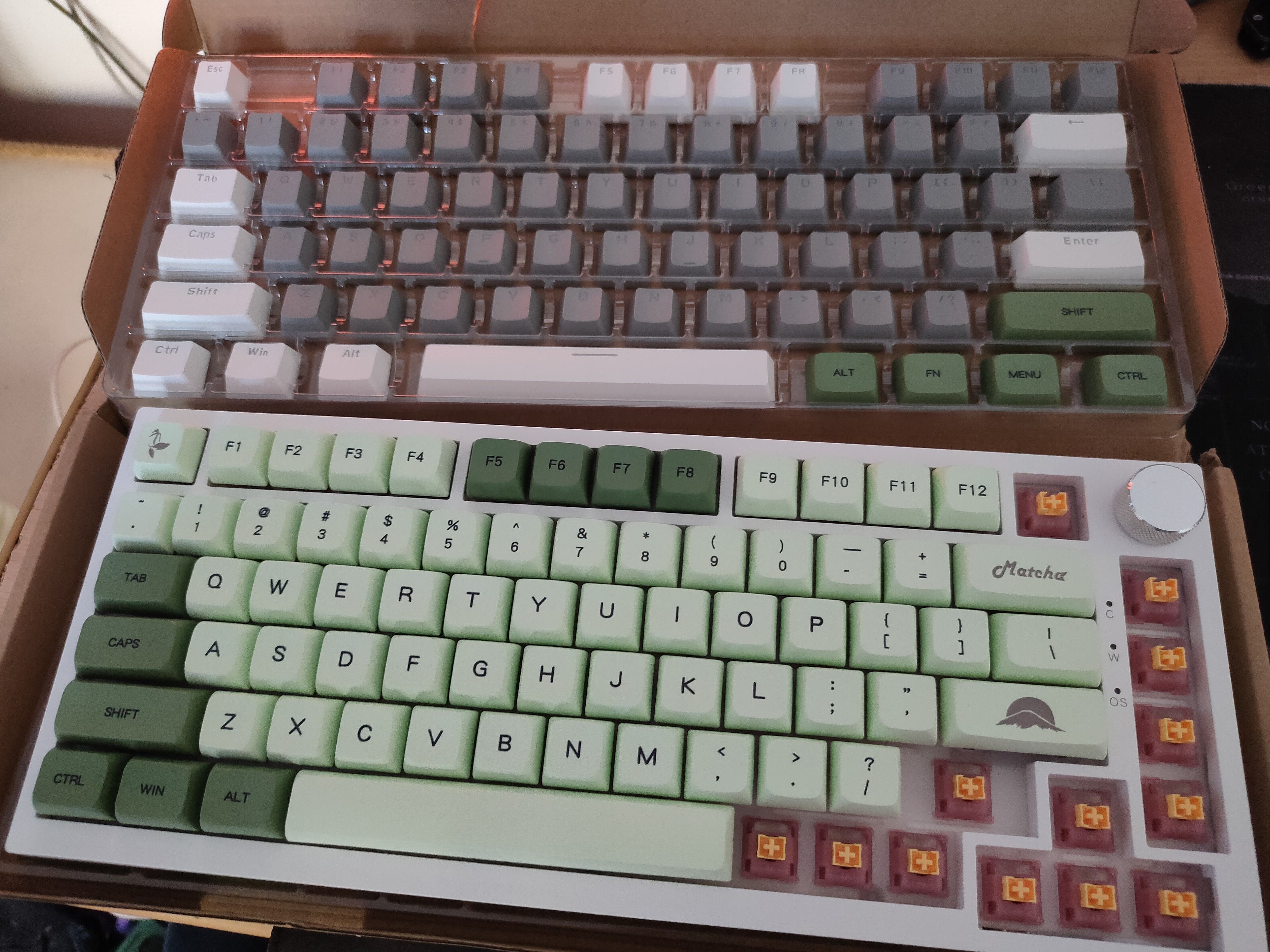 The Ajazz AK820 keyboard with custom green keycaps being installed and the stock keycaps above it.