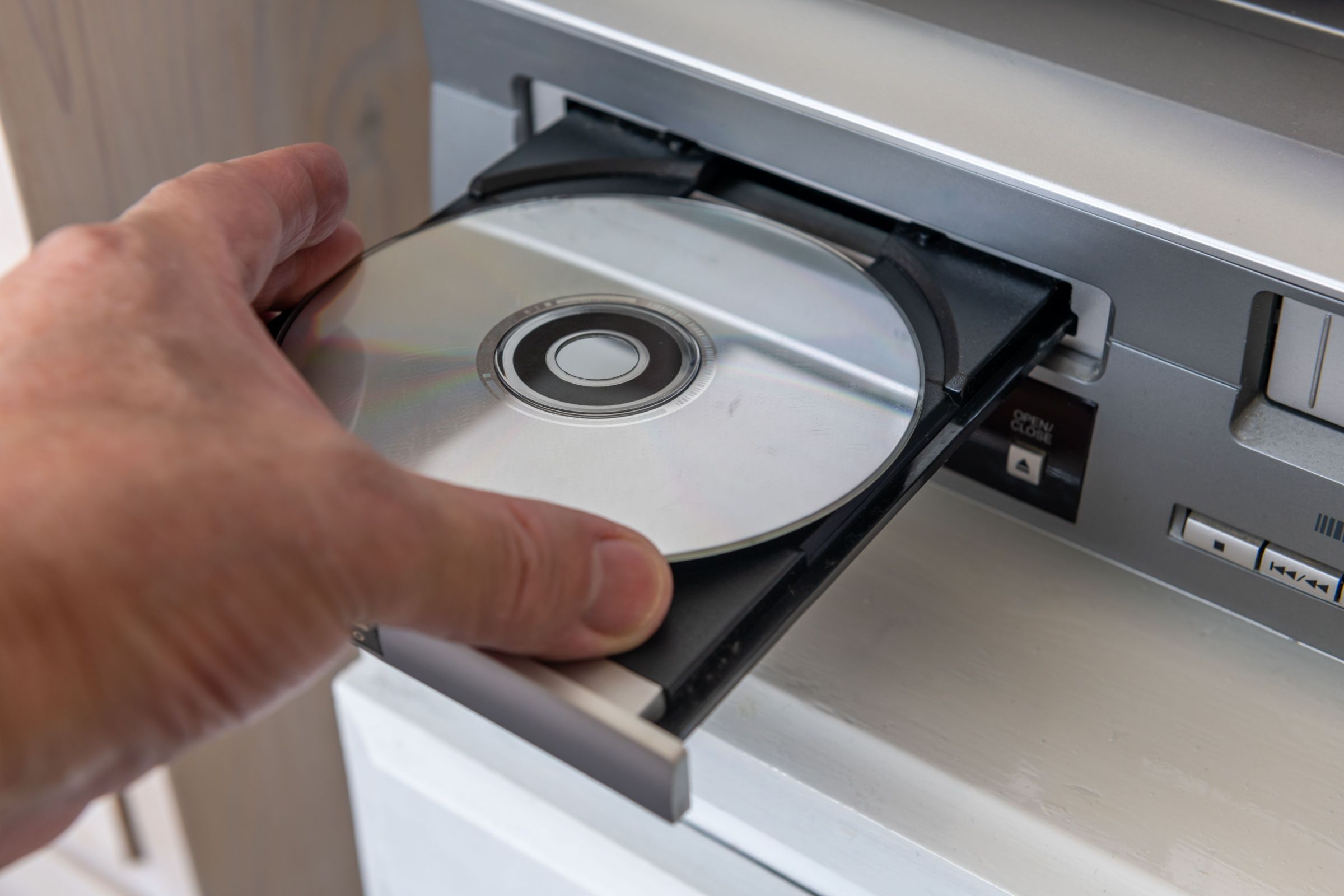 A person inserting a digital video disc into a DVD player.